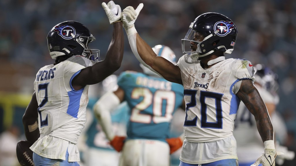 Two Tennessee Titans football players celebrating on the field, wearing white jerseys with blue accents, as they high-five each other during a game.