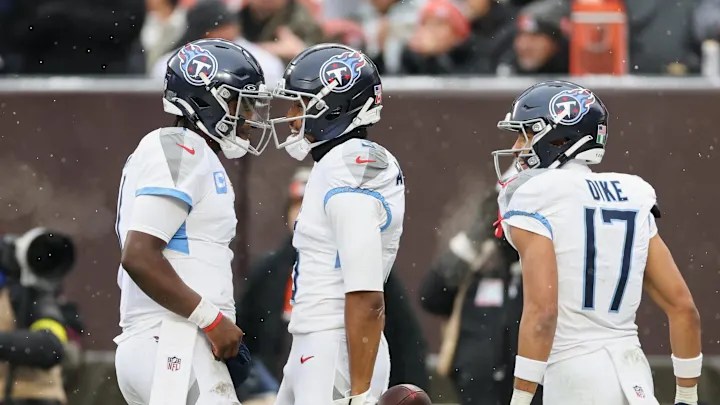 Three football players celebrating on the field in snowy conditions, wearing Tennessee Titans uniforms.